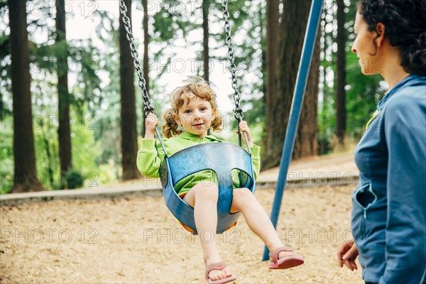 Caucasian mother pushing daughter on swing