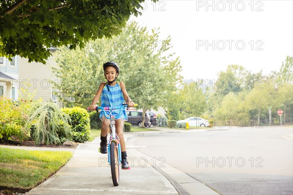 Mixed race girl riding bicycle on sidewalk