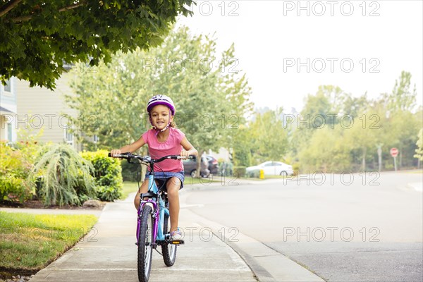 Mixed race girl riding bicycle on sidewalk