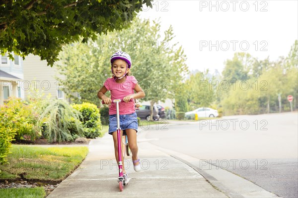 Mixed race girl riding scooter on sidewalk