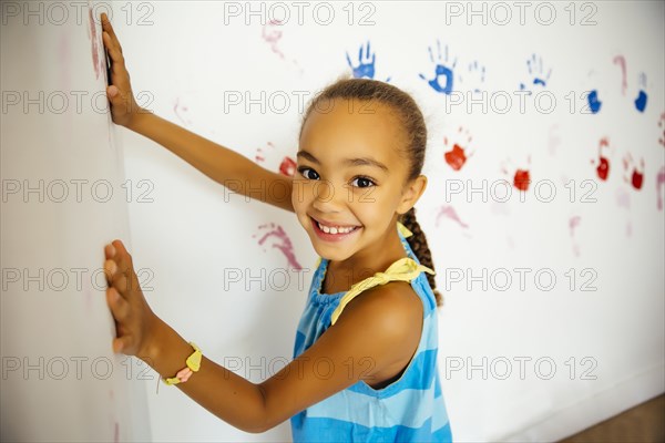 Mixed race girl making hand prints on wall