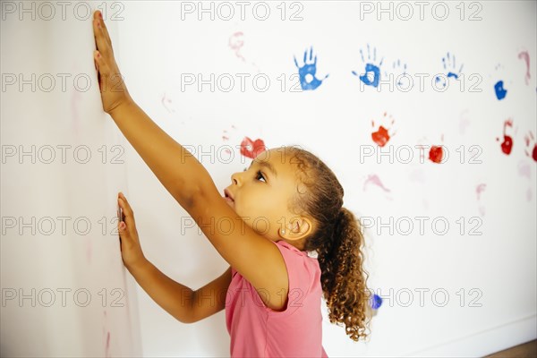 Mixed race girl making hand prints on wall