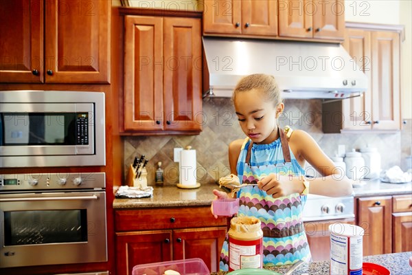 Mixed race girl scooping peanut butter in kitchen