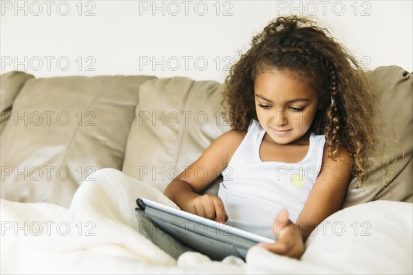 Mixed race girl using digital tablet on sofa