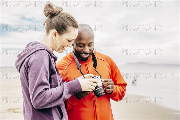 Couple reviewing digital photographs on beach