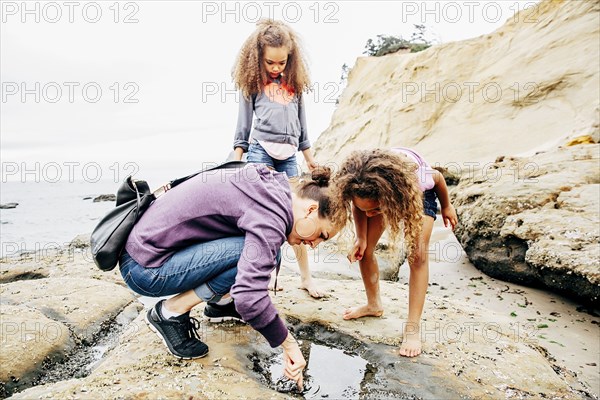 Mother and daughters examining tide pools on beach