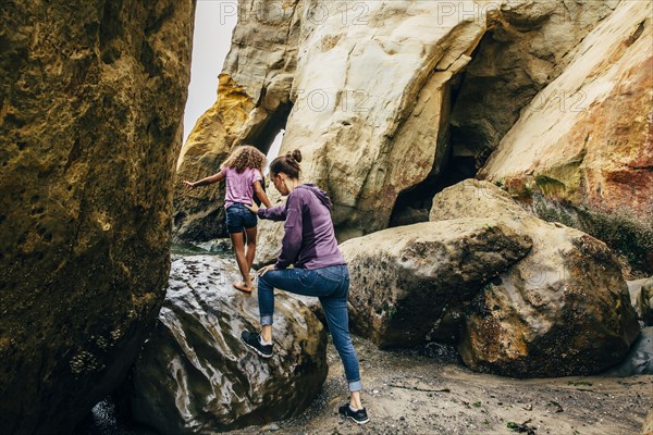 Mother and daughter climbing on beach rocks