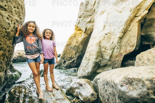 Mixed race sisters smiling on rocks