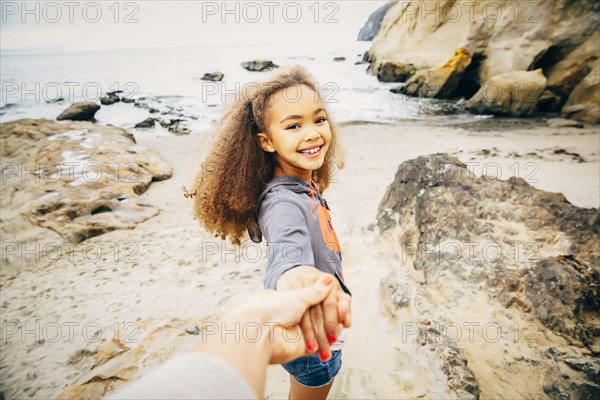 Girl pulling hand of mother on beach