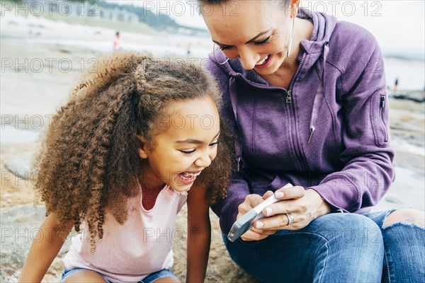 Mother and daughter using cell phone on beach