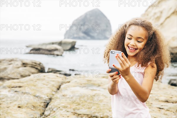 Mixed race girl using cell phone on beach