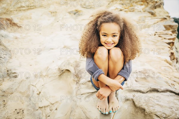 Mixed race girl hugging knees on rock