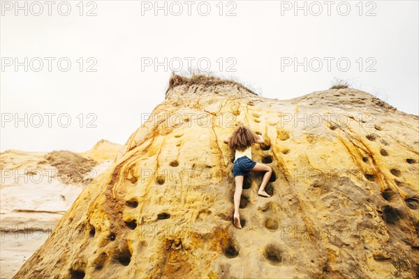 Mixed race girl climbing cliff rock