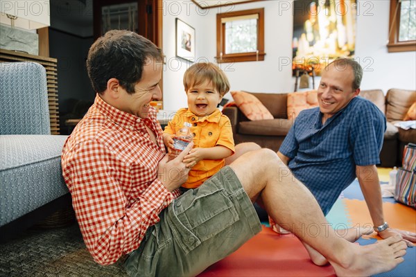 Gay fathers playing with baby son in living room