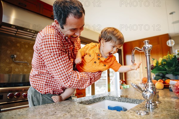Father and son playing with faucet in kitchen