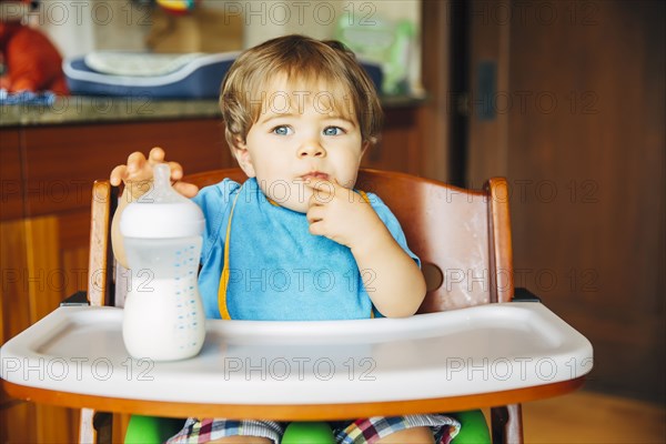 Mixed race baby boy drinking bottle in high chair