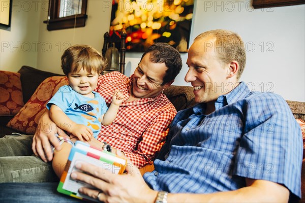 Gay fathers playing with baby son on sofa