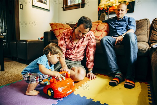 Gay fathers playing with baby son in living room