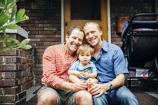 Gay fathers holding baby son on front stoop