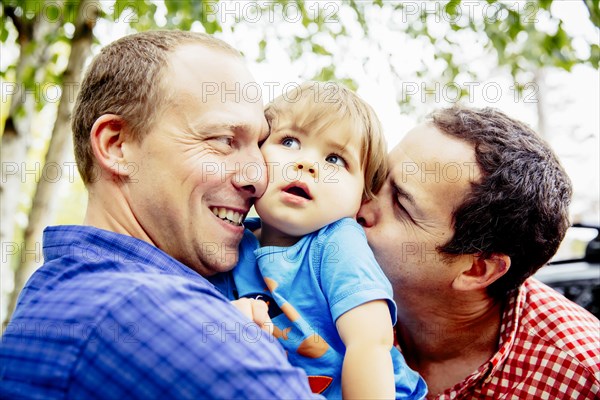 Gay fathers kissing baby son outdoors