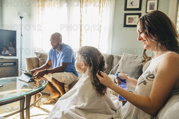 Mother styling hair for daughter in living room