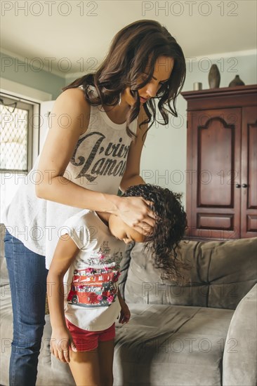 Mother styling hair for daughter in living room