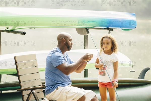 Father baiting fishing hook for daughter at lake