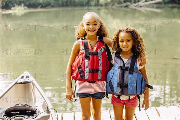 Mixed race sisters wearing life jackets at lake