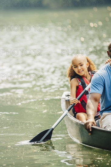 Father and daughter rowing canoe in lake