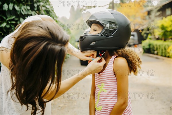 Mother fastening helmet on daughter