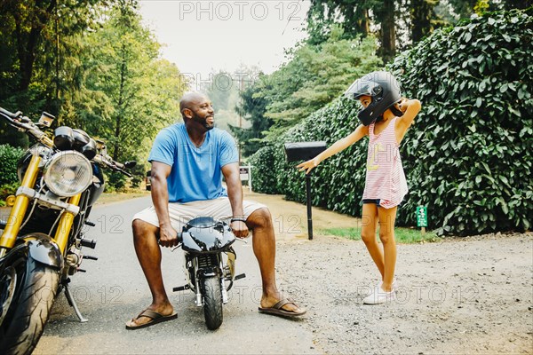 Father sitting on miniature motorcycle near daughter