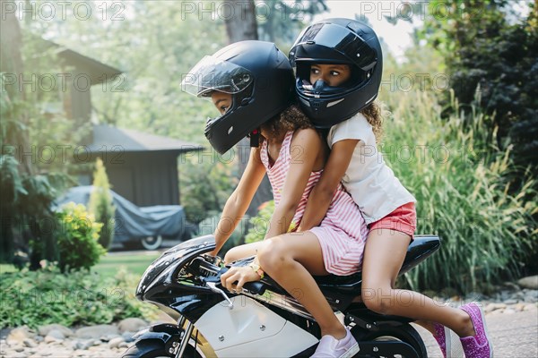 Mixed race sisters riding miniature motorcycle