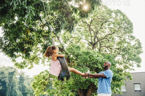 Father pushing daughter on tire swing