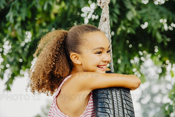 Mixed race girl smiling in tire swing