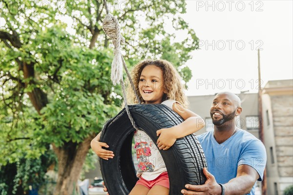 Father pushing daughter on tire swing