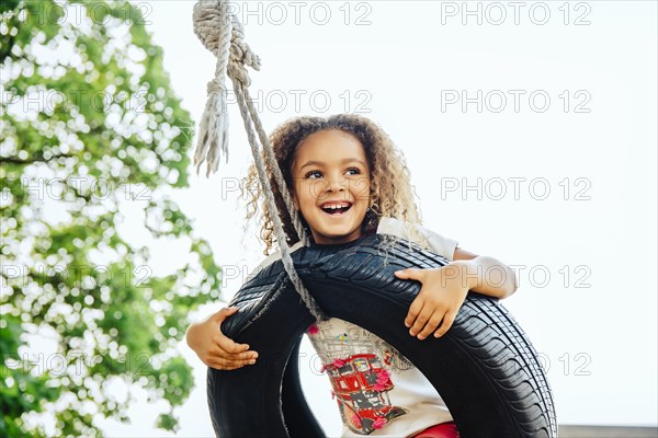 Mixed race girl smiling in tire swing