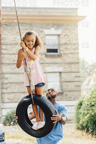 Father pushing daughter on tire swing