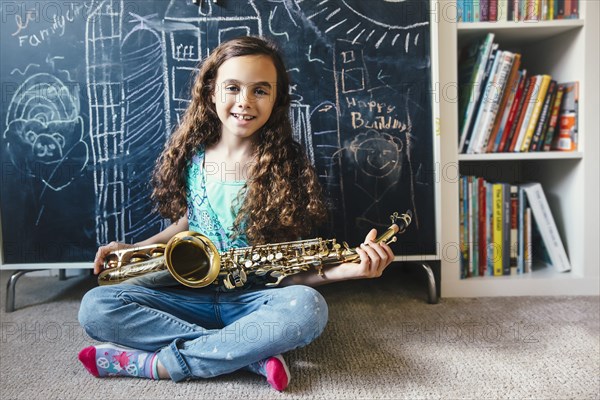 Mixed race girl holding saxophone on floor