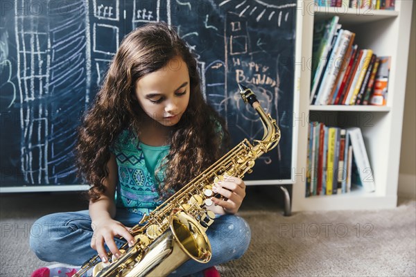 Mixed race girl playing saxophone on floor