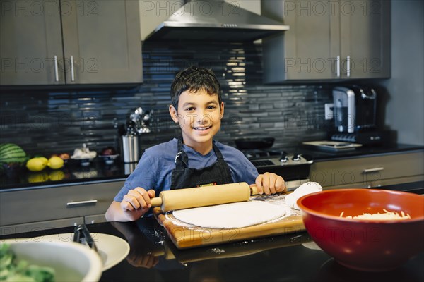 Mixed race boy rolling dough in kitchen