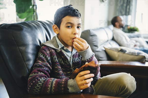 Mixed race boy eating in armchair
