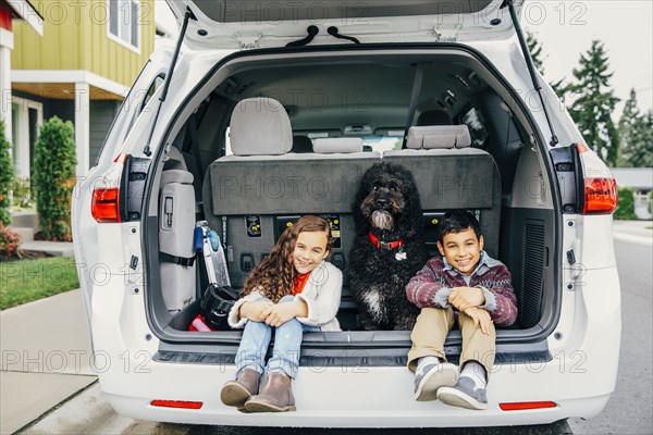 Mixed race children sitting with dog in car hatch