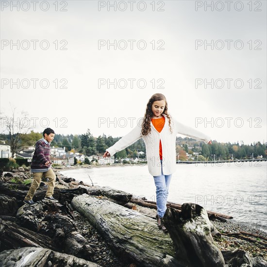 Mixed race children climbing on logs at lake