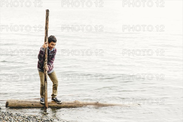 Mixed race boy playing on log in lake