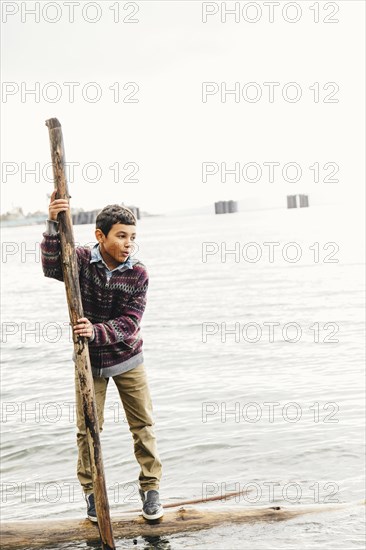 Mixed race boy playing on log in lake