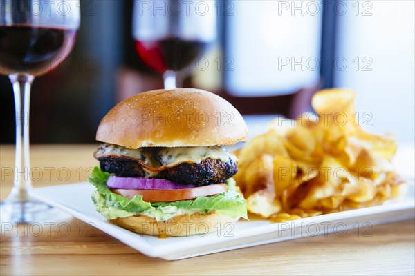 Plate of cheeseburger and chips with wine