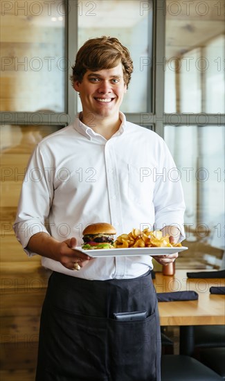 Caucasian waiter carrying cheeseburger and chips in cafe