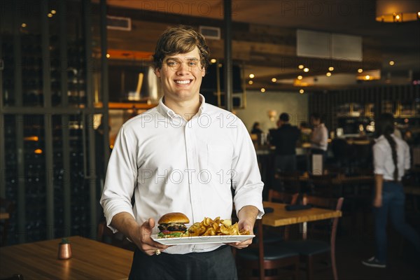 Caucasian waiter carrying cheeseburger and chips in cafe