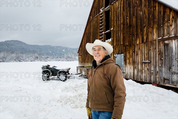 Caucasian farmer smiling near snowy barn