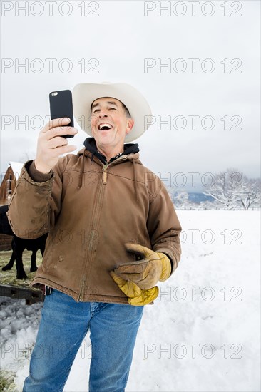 Caucasian farmer using cell phone in snowy field